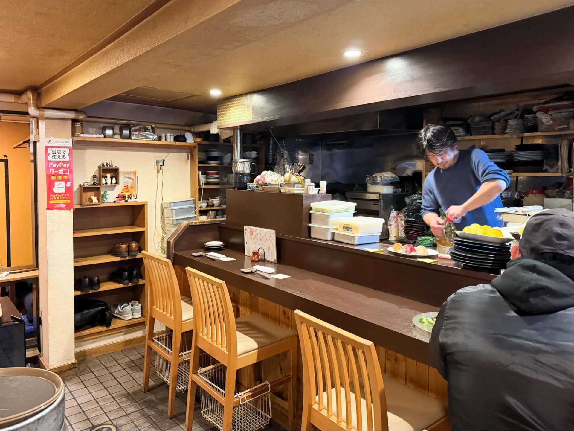 青森県八戸市のたぬき小路にある「暖だん」のカウンター席と、店主の竹内広貴さん