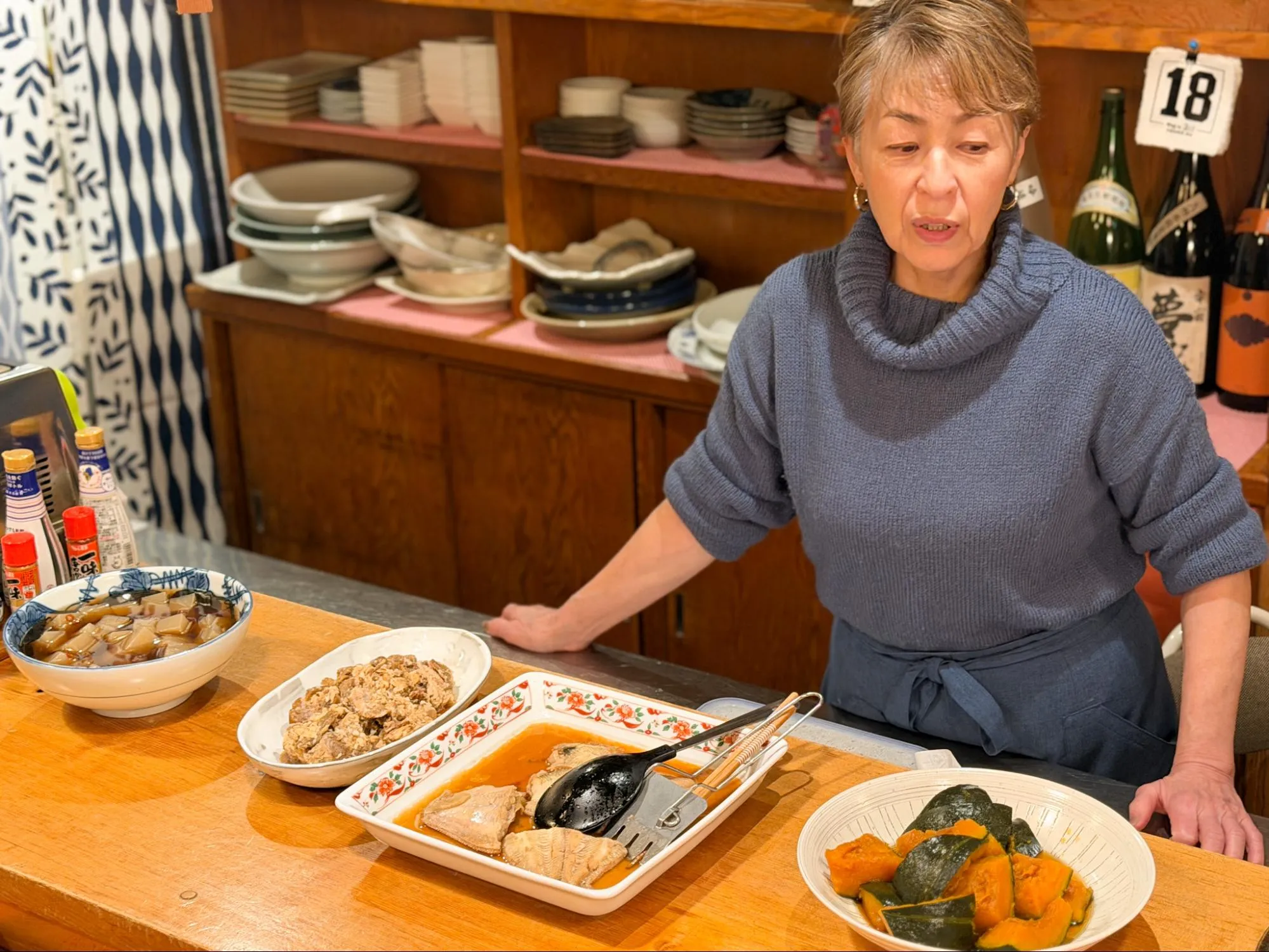 「山き」の、一枚板のカウンター。大皿に盛り付けられたおばんざいがずらりと並び、そこから食べたいものを注文することができます。