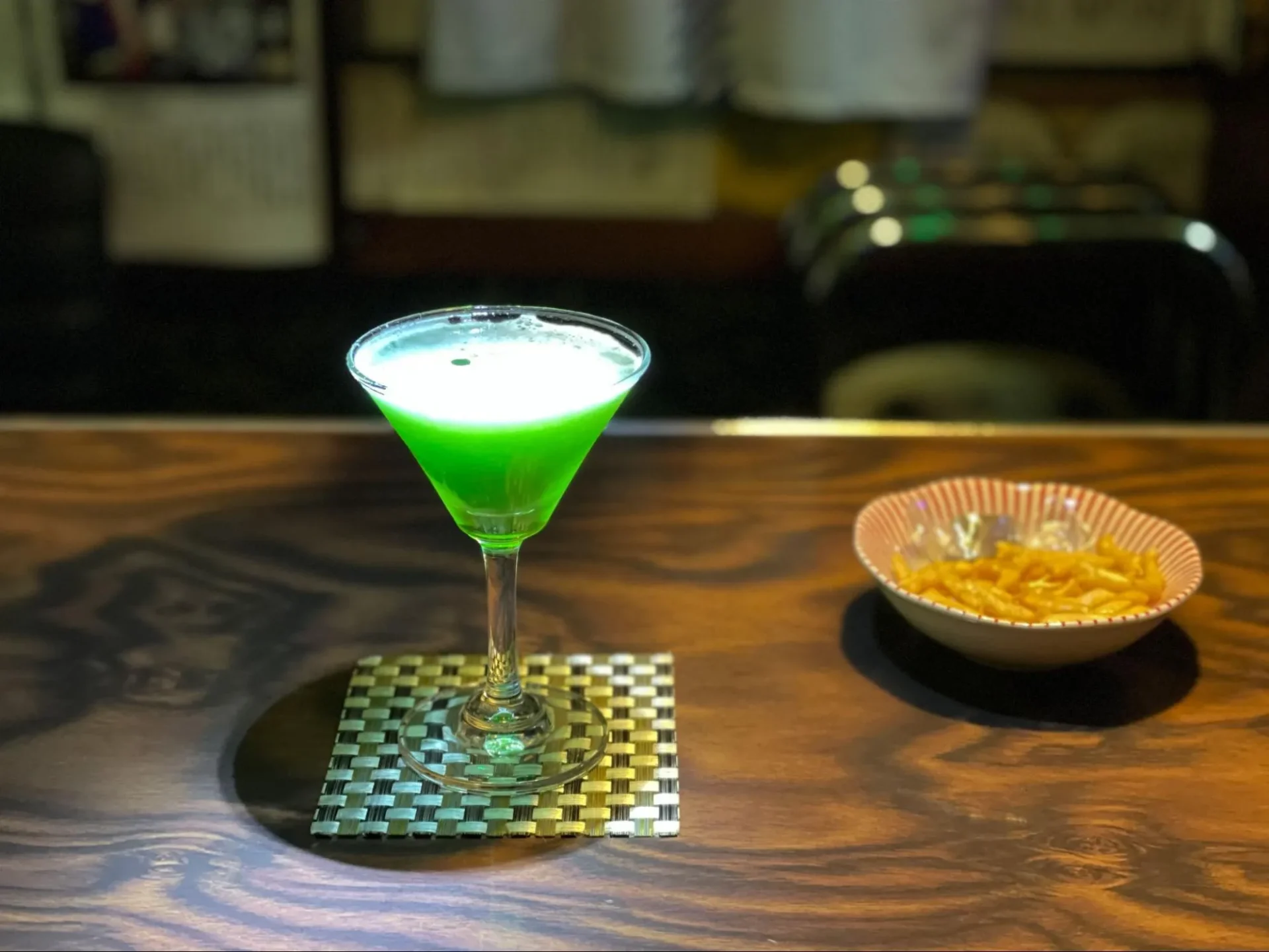 「洋酒喫茶 プリンス」の、日本酒とジン、グリーンティーリキュールで種差の天然芝を再現した「種差」。右にあるのはお通しとして提供されるスナック「こざかなくん」とチョコレート。